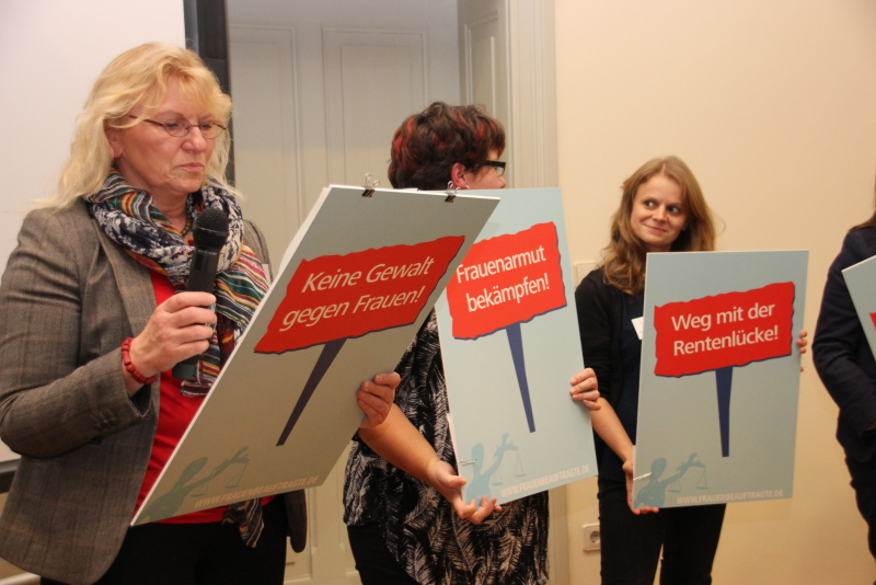 Drei Mitglieder des Frauenbeirates halten Schilder mit Forderungen in ihren Händen.