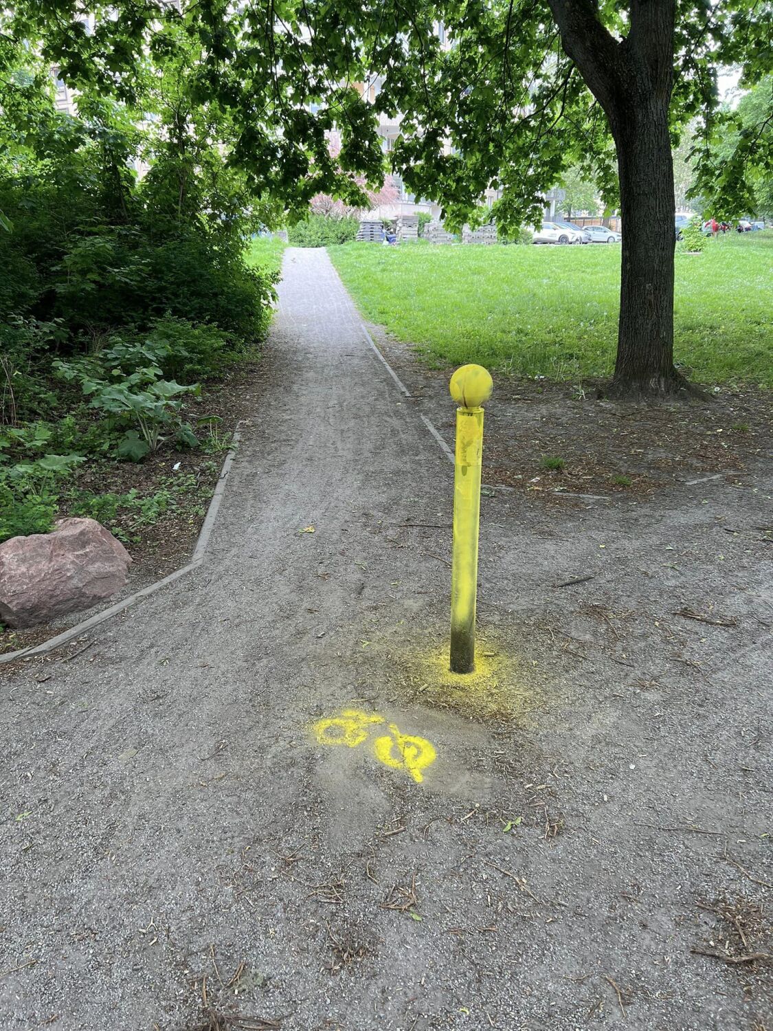 Auf einem Weg steht ein Poller. Der Poller wurde mit gelber Kreidespray besprüht, da er eine Unfallgefahr darstellt. Er unterscheidet sich farblich kaum von seiner Umgebung.