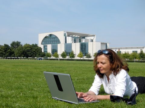 Frau liegt mit Laptop auf Wiese vor Bundeskanzleramt