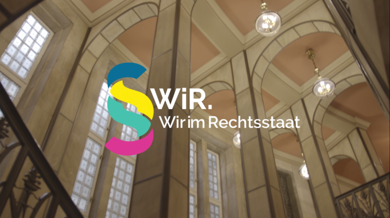 Das Logo des Projekts „WiR – Wir im Rechtsstaat“ vor einem Gebäudehintergrund