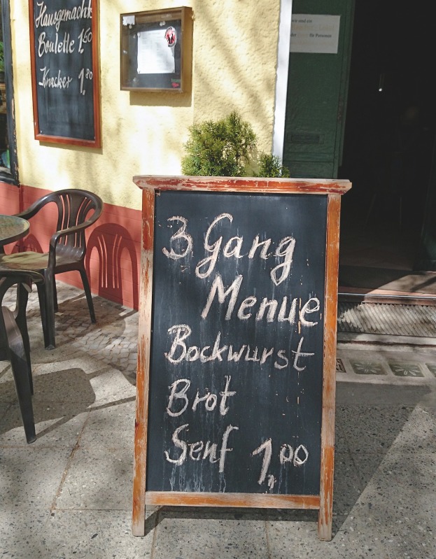 Tafel mit Ankündigung eines 3 Gang Menue: Bratwurst, Brot, Senf