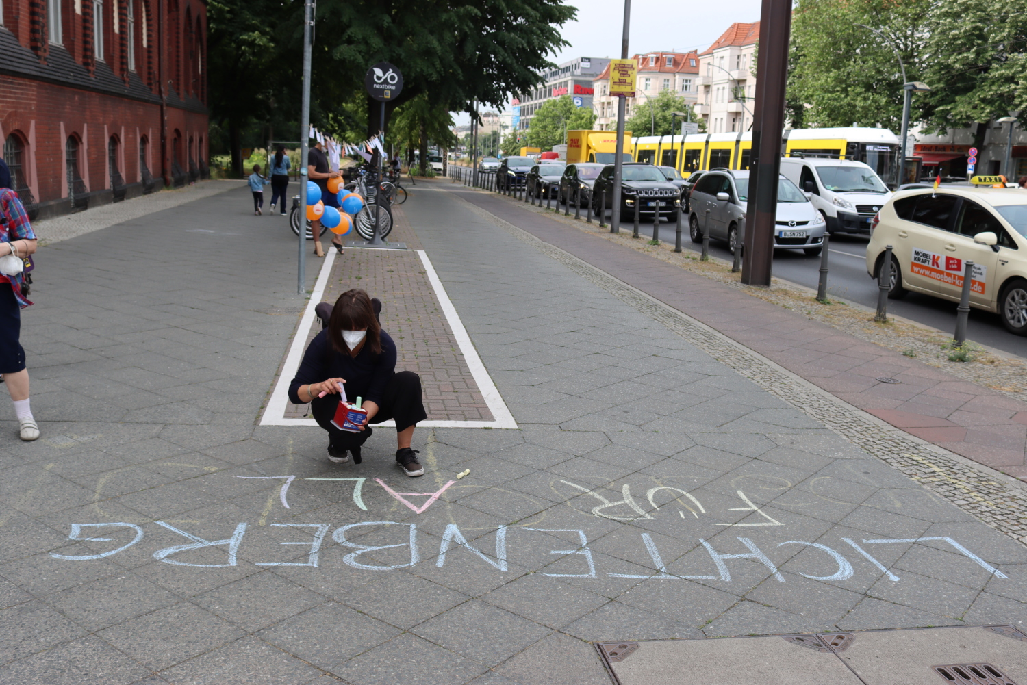 Annabel Haas-Krahé zeichnet auf dem Gehweg neben dem Rathaus mit Straßenkreide den Schriftzug: "Lichtenberg für alle!".