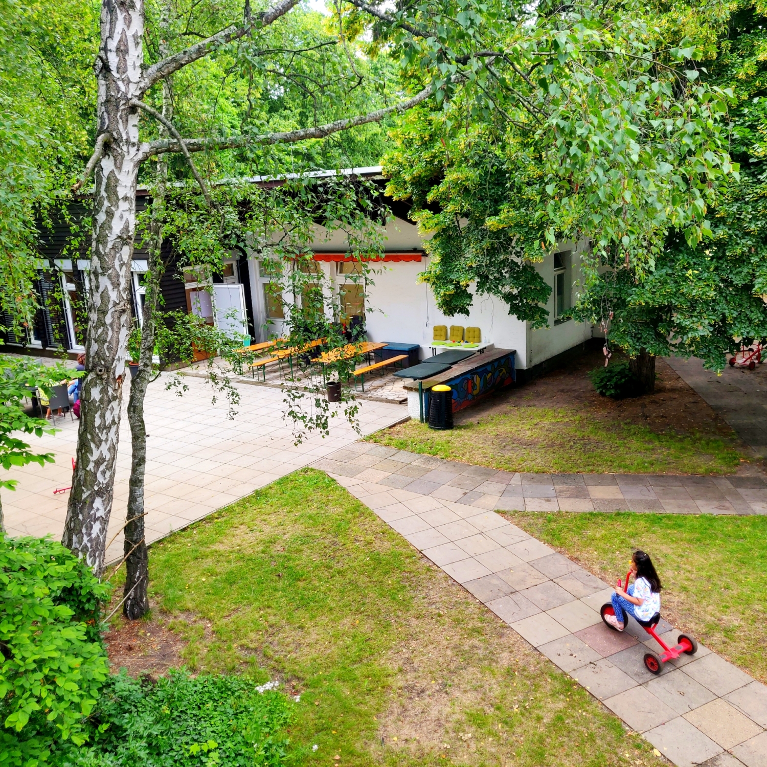 Sicht von Oben auf Außengelände und Nebengebäude Haus am See, ein Mädchen links fährt auf einem Dreirad