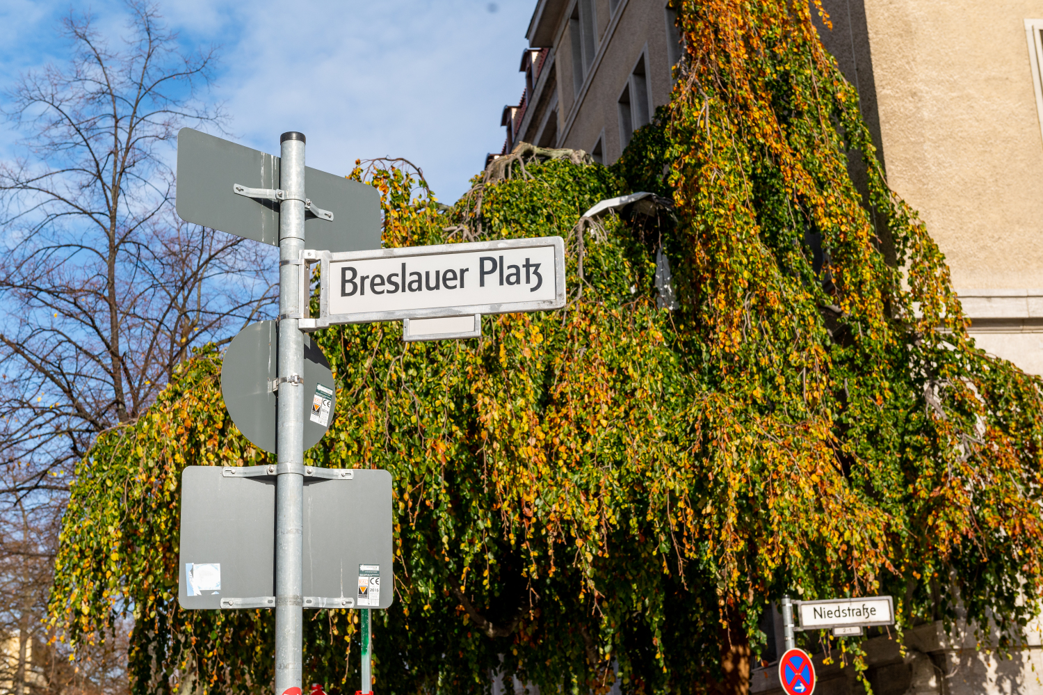 Ein Straßenschild mit der Aufschrift "Breslauer Patz". Im Hintergrund sind Bäume und ein blauer Himmel zu sehen.