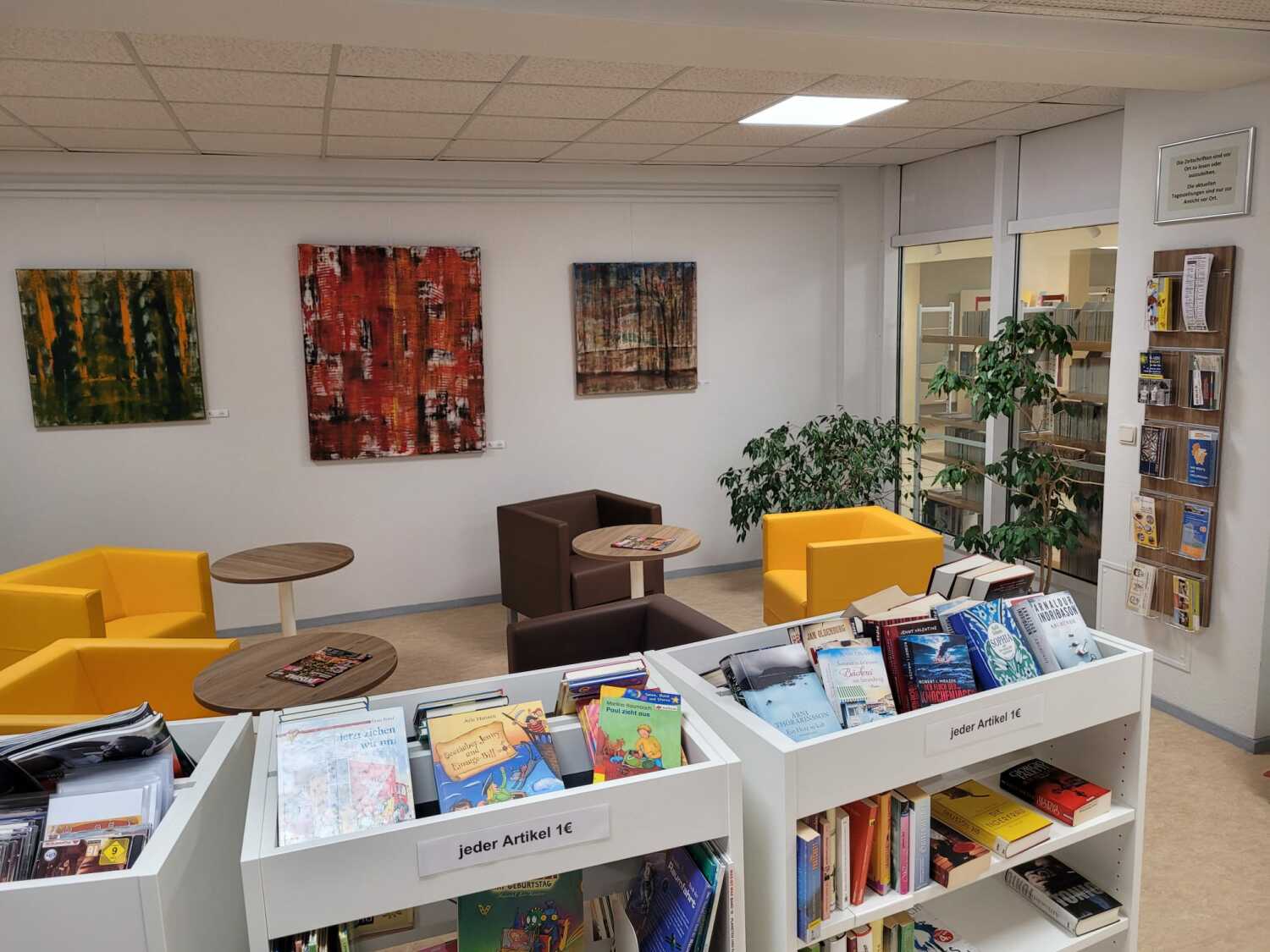 Blick auf die Leseecke mit gelben und braunen Sesseln, im Vordergrund der Büchertrödel