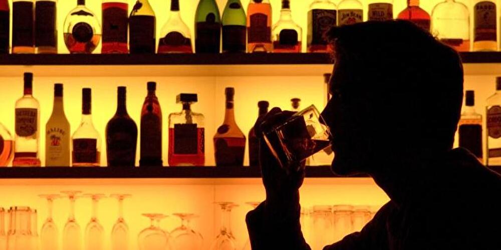 Ein Bar-Besucher sitzt trinkend neben einem Flaschenregal