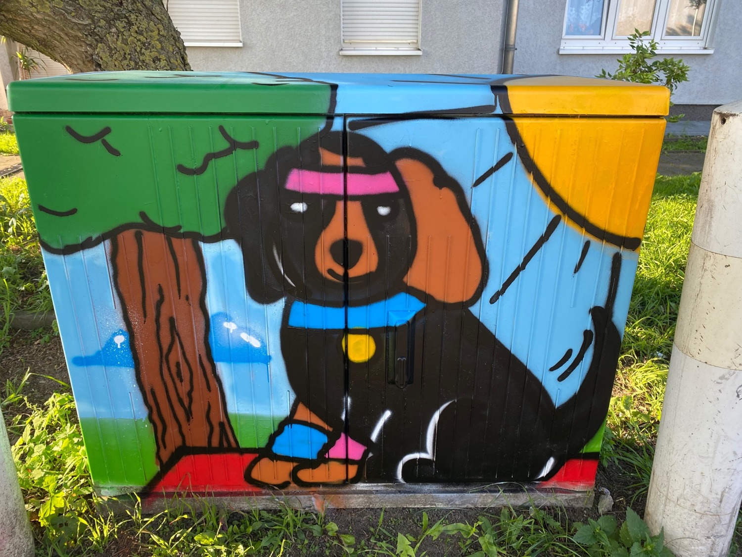 Stromkasten bemalt mit einem Hund, einem Baum und einer Sonne