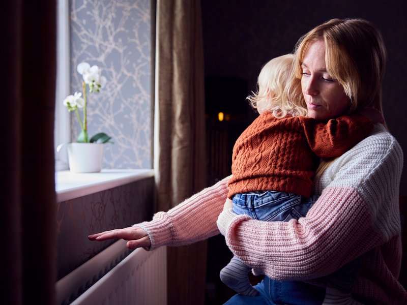 Mutter mitkleinem Kind auf dem Arm schaut traurig aus dem Fenster