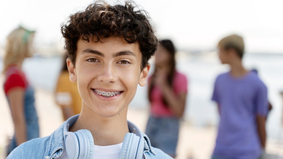 Lächelnder dunkelhaariger Jugendlicher mit Zahnspange und Kopfhörern um den Hals