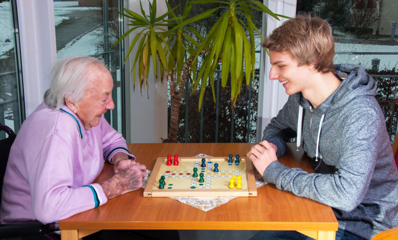 Ein Jugendlicher spielt mit einer Seniorin ein Brettspiel