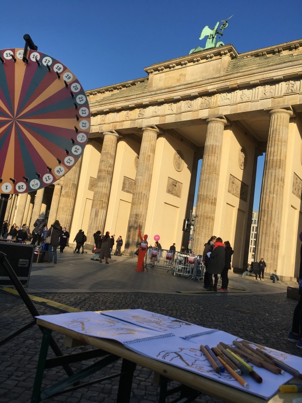 Ein Kindertisch mit Stiften und dem GPR-Malbuch, daneben das Glücksrad und im Hintergrund das Brandenburger Tor