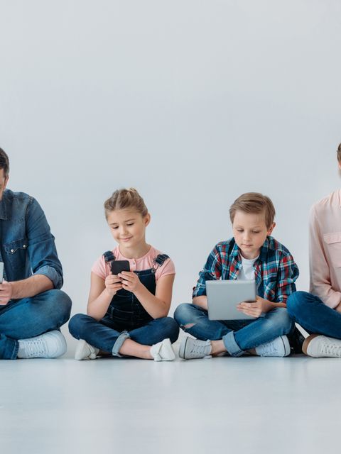Eltern mit zwei Kindern sitzen auf dem Boden und halten jeweils ein Handy oder ein Tablet