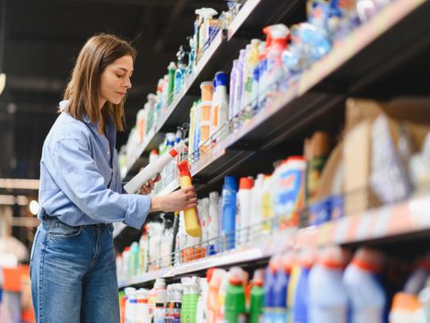 Frau kauft im Supermarkt ein und schaut sich Reinigungsmittel im Regal an