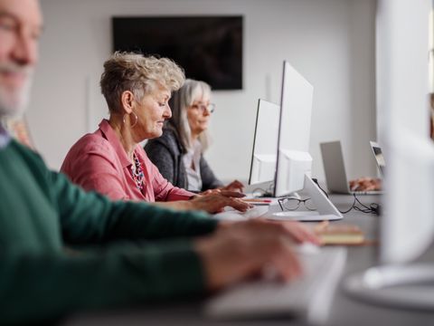 Gruppe von älteren Menschen sitzt an Computer, Profilansicht