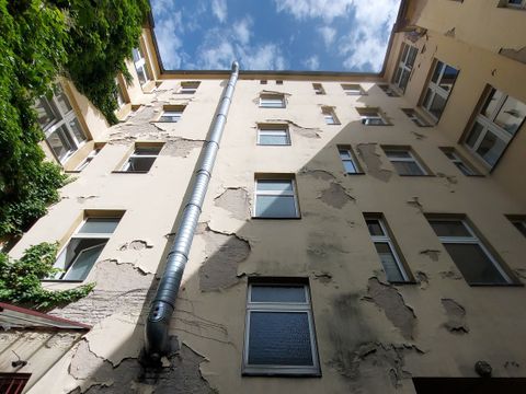 Innenhof eines Hauses mit sehr kaputter Hauswand, Blick nach oben in den Himmel, linke Hauswand ist bewachsen