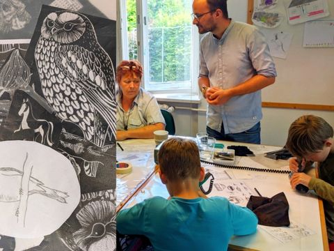 Tiermotive als Vorlagen für die Glasgravur, Susanne Fabian (links) und Dachsbauleiter Bastian Weber (rechts) mit zwei Kindern, die gerade Gläser gravieren (Bild: BA Reinickendorf)