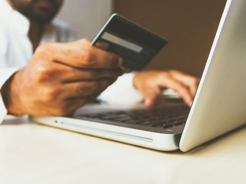 Mann am Laptop hält Bezahlkarte in der Hand und tippt etwas ab