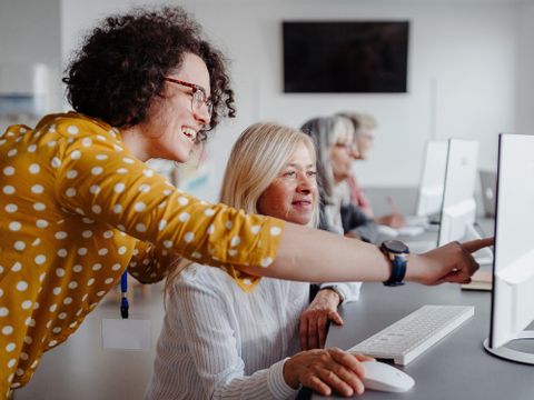 ältere Frau lernt Umgang mit moderner Technologie am Computer von Lehrkraft, Profilansicht
