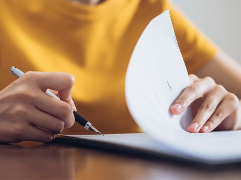Eine Frau unterzeichnet ein Dokument und hält dabei den Stift in der Hand
