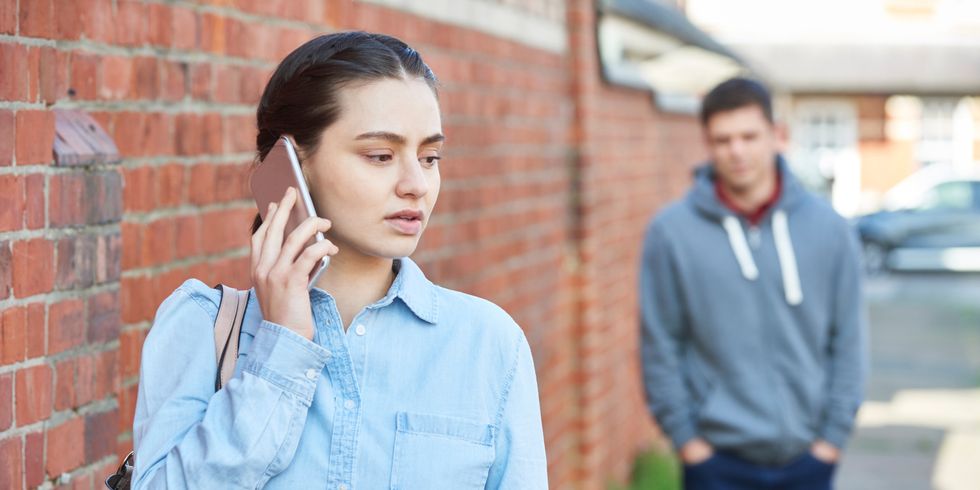 Häusliche Gewalt - eine Frau ruft mit dem Handy nach Hilfe, weil sie von einem Mann gestalkt wird