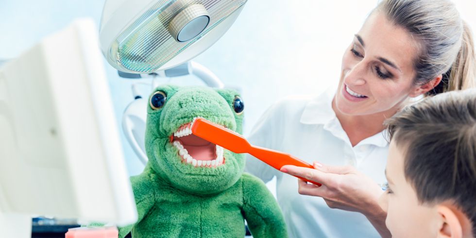 Boy looking at doctor brushing the dinosaur's teeth in clinic