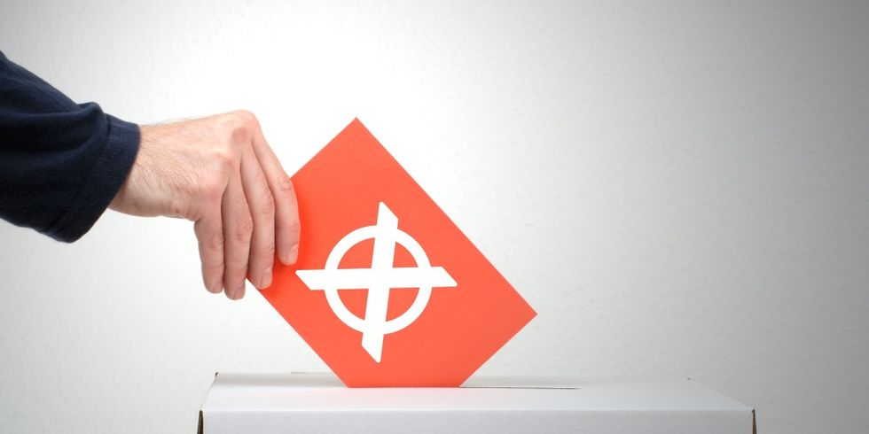 Hand, die einen Umschlag in eine Wahlurne steckt