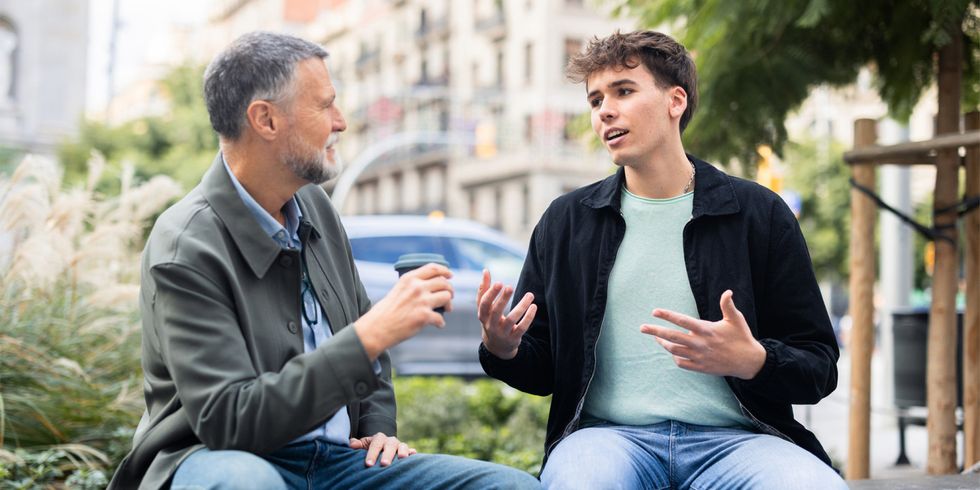 Jugendlicher und Erwachsener diskutieren auf einer Bank am Straßenrand