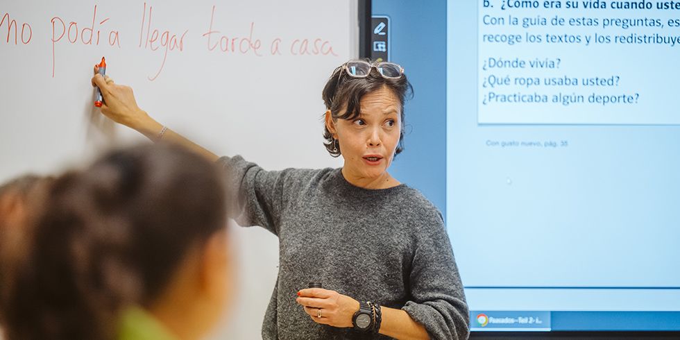Kursleiterin Alicia Villasenor steht am Whiteboard, zeigt auf ein spanisches Wort und schaut in den Unterrichtsraum