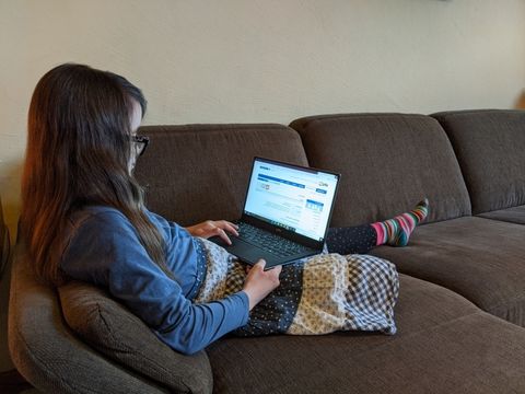 Kind sitzt auf dem Sofa mit einem Laptop auf dem Schoß