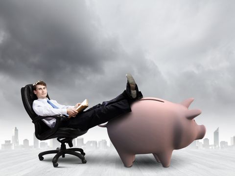 Ein Mann sitzt entspannt in einem Chefsessel, seine Beine liegen ausgesteckt auf einem großen Sparschwein