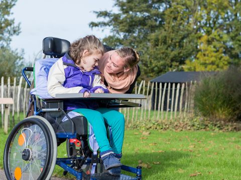 eine Frau beugt sich herunter zu einem Mädchen im Rollstuhl