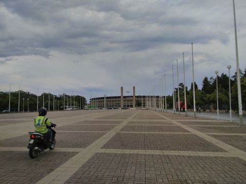 Der olympische Platz mit dem Stadion im Hintergrund, ein Rollerfahrer im Vordergrund