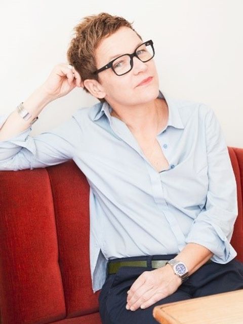 Bildvergrößerung: Eine Frau sitzt leicht angelehnt auf einer roten Samtcouch. Sie trägt eine schwarze Brille, hat kurze Haare und sieht direkt in die Kamera.
