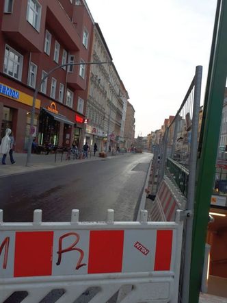 Bildvergrößerung: Foto: Ein rot-weißer Bauzaun im Vordergrund, rechts abgezäunte Baustelle, links Blick auf eine leere Straße mit Geschäften