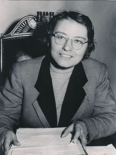 Eine Frau sitzt am Schreibtisch mit eine Stapel Unterlagen