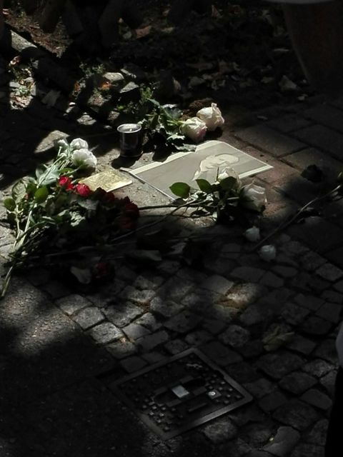Bildvergrößerung: Foto von verlegten Stolpersteinen neben denen weiße und rote Rosen liegen.