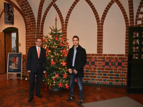 Bildvergrößerung: Bezirksbürgermeister Igel (l.) und Herr Gilke vom Verein Schenk doch mal ein Lächeln e.V. vor dem Wunschbaum im Rathaus Köpenick