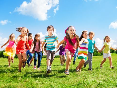 Eine Gruppe von Kinder rennt fröhlich über eine Wiese