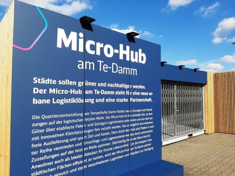 Bildvergrößerung: Ein Schild vor dem Micro-Hub am Te-Damm. Aufschrift: Städte sollen grüner und nachhaltiger werden. Der Micro-Hub am Te-Damm steht für eine neue urbane Logistiklösung und eine starke Partnerschaft.