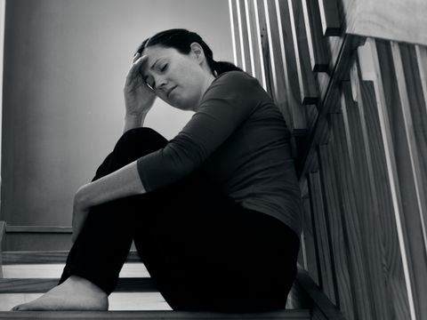 Frau sitzt mit geschlossenen Augen auf Treppenstufen mit einer Hand am Kopf