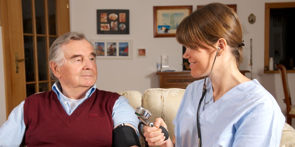 Pflegerin misst Blutdruck eines Senioren in seinem Zuhause