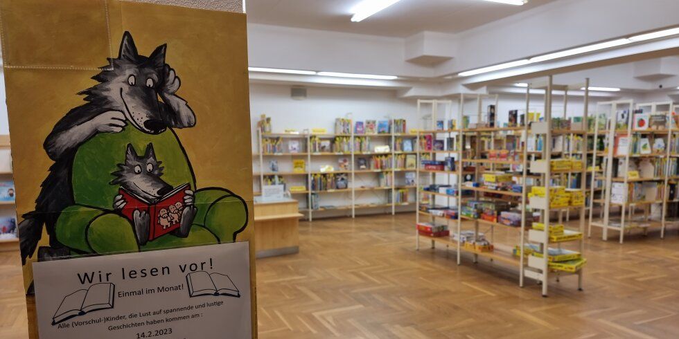 Blick in die Kinderbibliothek mit Veranstaltungsplakat zur Reihe "Wir lesen vor!" an einer Säule