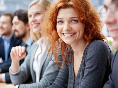 Lächelnde junge Frau sitzt mit vier weiteren lächelnden Menschen an einem Konferenztisch