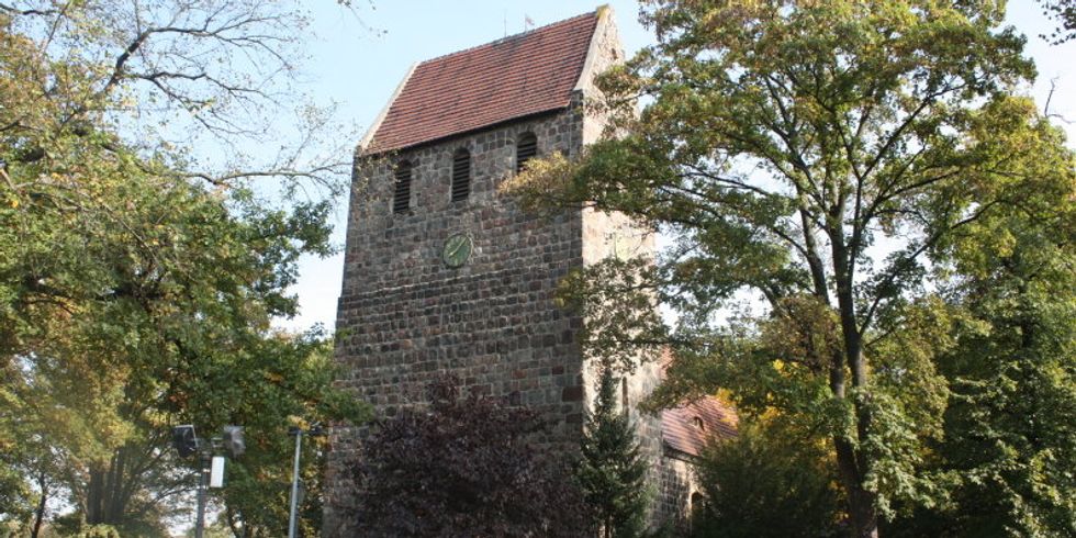 Gemauerter Kirchturm, umgeben von Bäumen