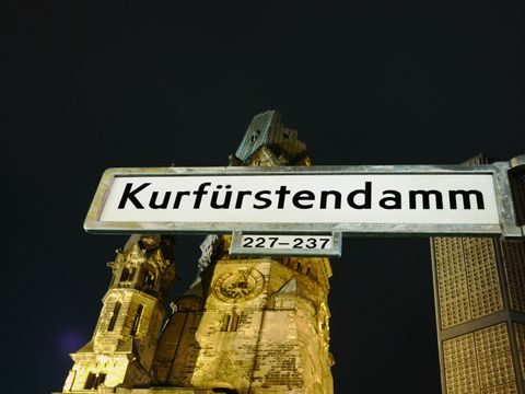 Straßenschild mit der Aufschrift "Kurfürstendamm", im Hintergrund die Kaiser-Wilhelm-Gedächtniskirche