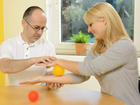 Ein Ergotherapeut zeigt seiner Patientin Übungen mit einem Noppenball
