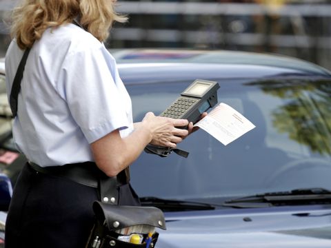 Eine Frau im Uniform tippt auf einem mobilen Gerät und steht dabei vor einem Auto