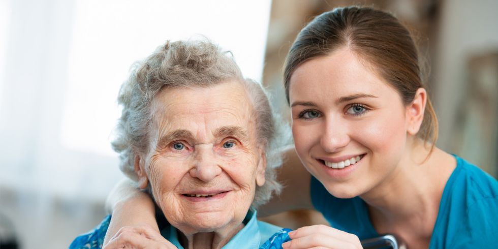 Junge Pflegerin umarmt lächelnde Seniorin