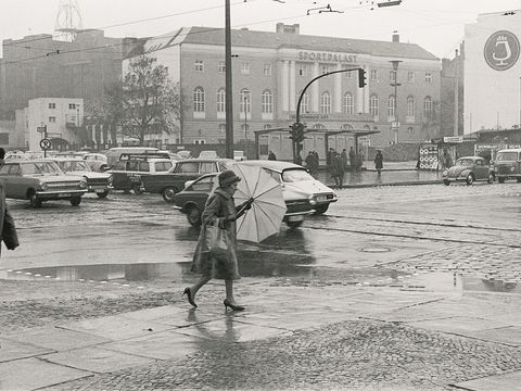 Schwarzweißfoto Frau mit Regenschirm auf Kreuzung vor Sportpalast