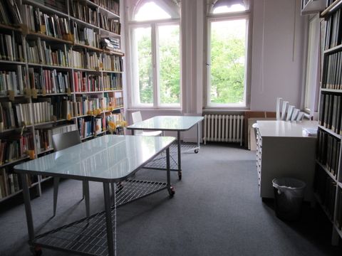 Raum mit Tischen, Stühlen und vollen Bücherregalen